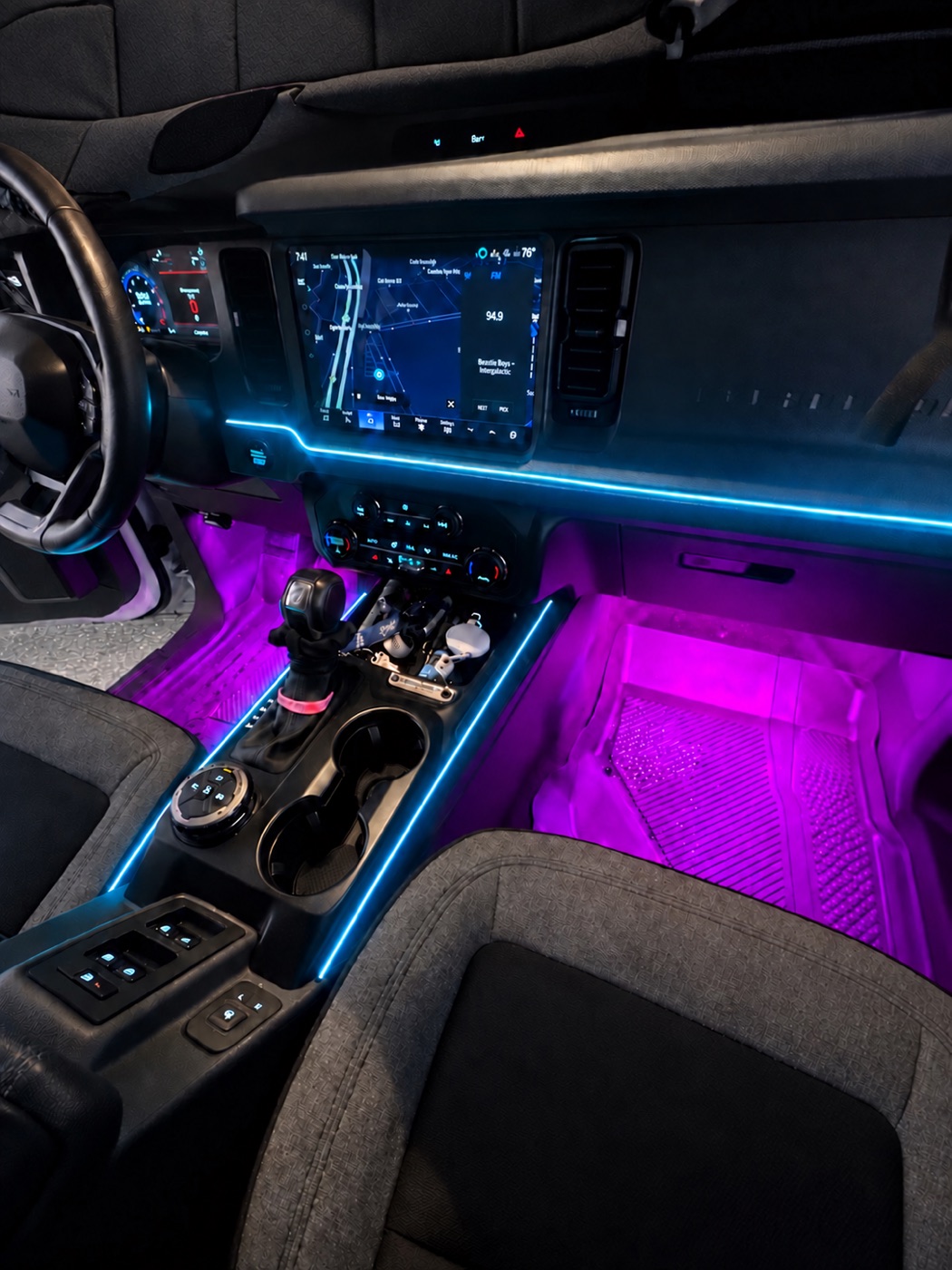 Cyan dashboard and console lighting with purple footwell lighting in a Ford Bronco; AI-enhanced photo